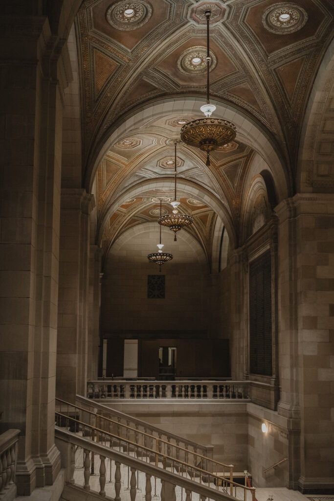 Architectural detail of Crew Collective & Café in Old Montreal, captured by wedding photographer Jeff Gagnon, showcasing its grand staircase, ornate vaulted ceilings with intricate patterns, and elegant chandeliers.