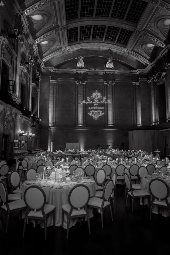 Black and white photograph of an elegant wedding reception at Théâtre St-James in Montreal, captured by wedding photographer Jeff Gagnon, featuring round tables with candlelit centerpieces, ornate high ceilings, and a custom monogram projection on the grand wall.